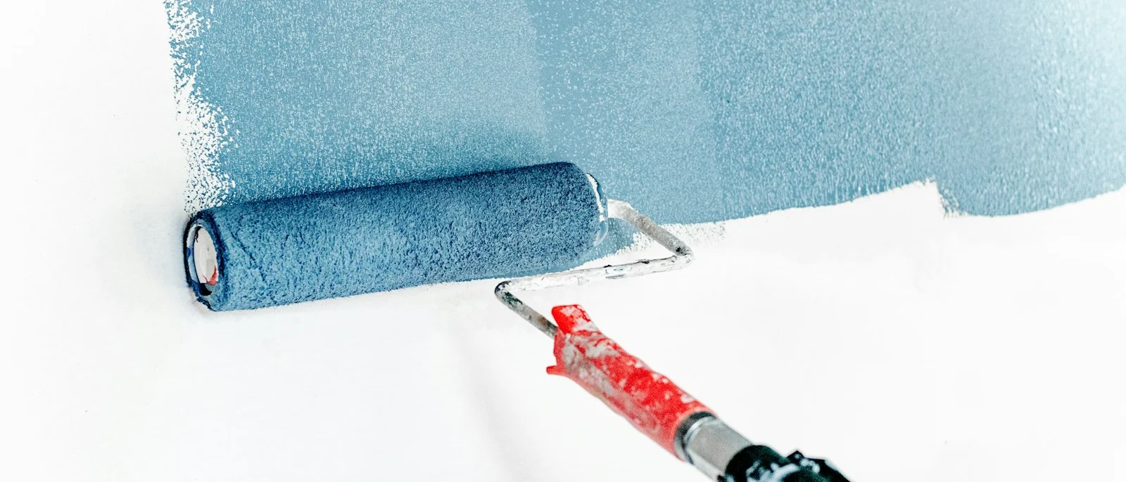 Rodillo aplicando pintura azul sobre una pared blanca